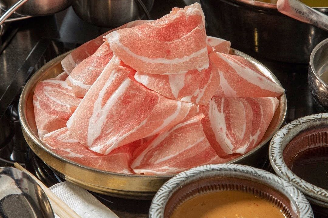 Thin-sliced pork in a brass bowl beside Mokkoji's dipping sauces